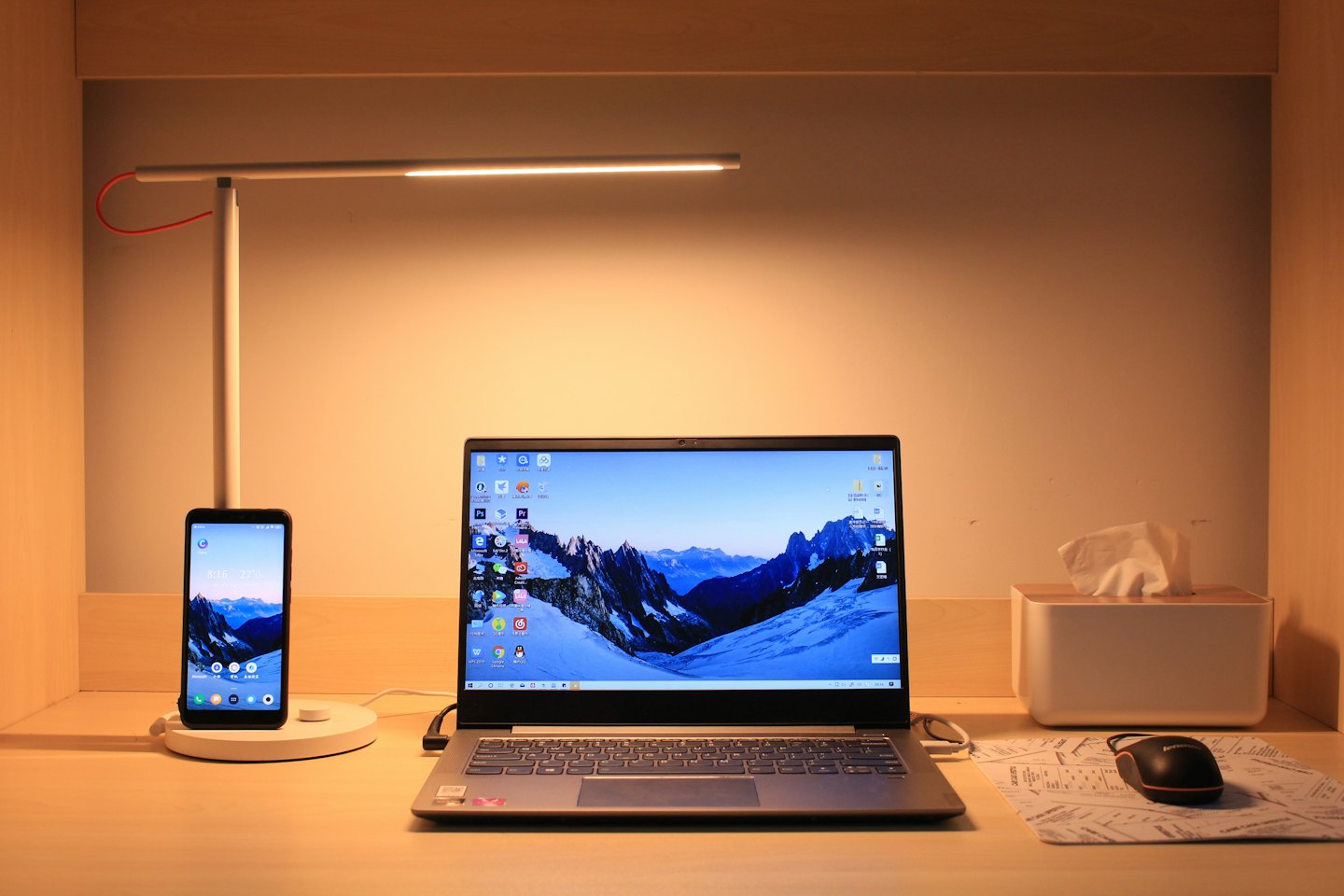 Laptop i smartfon ładujące się na drewnianym biurku.